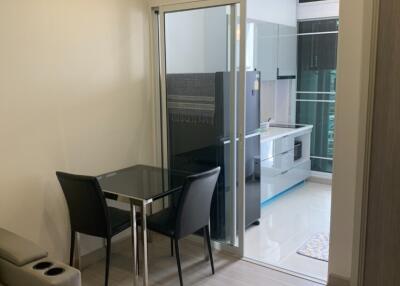 Small living area with a glass table and two chairs, adjacent to a modern kitchen