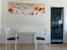 Small dining area with white table and chairs, floral wall art, and partial view of kitchen