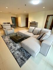 Modern living room with beige sofa and armchairs, glass coffee table, and dining area in the background