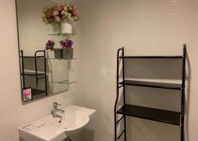 Modern bathroom with white tiles, a sink, mirror, shelving unit, and flowers