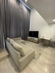 Modern living room with beige sofa, flat-screen TV, and tall curtains