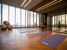 A spacious fitness room with yoga mats and exercise balls, featuring a city view from large windows