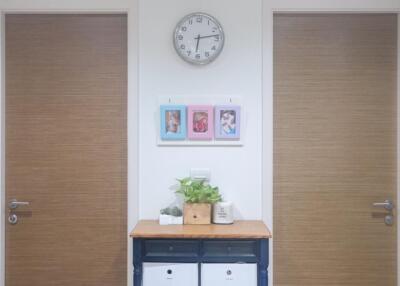 Hallway with two wooden doors, a clock, and a console table decorated with plants and photo frames