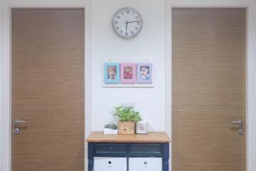 Hallway with two wooden doors, a clock, and a console table decorated with plants and photo frames