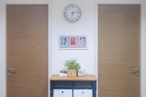 Hallway with two wooden doors, a clock, and a console table decorated with plants and photo frames