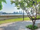 View of a riverside outdoor area with green landscaping and city skyline