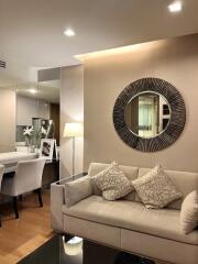 Modern living room with a sofa, decorative pillows, a lamp, and a large round mirror