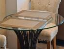 Small round glass dining table with two upholstered chairs