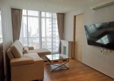 Modern living room with sofa, coffee table, wall-mounted TV, and large windows