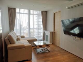 Modern living room with sofa, coffee table, wall-mounted TV, and large windows