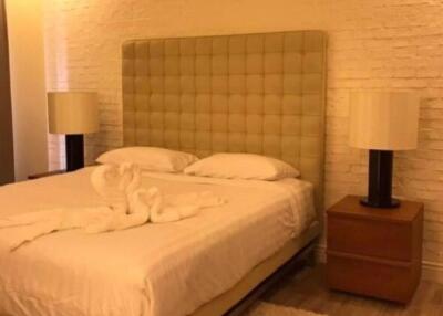 Bedroom with a large bed, two bedside tables with lamps, and textured white brick wall.