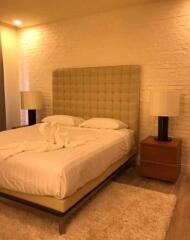 Bedroom with a large bed, two bedside tables with lamps, and textured white brick wall.