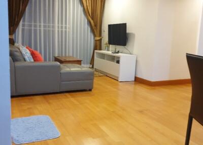 Living room with wooden flooring, gray sectional sofa, wall-mounted TV, white TV console, and large curtains