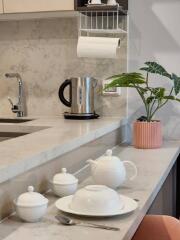 Modern kitchen counter with tea set, kettle, and green plant on marble surface