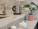 Modern kitchen counter with tea set, kettle, and green plant on marble surface