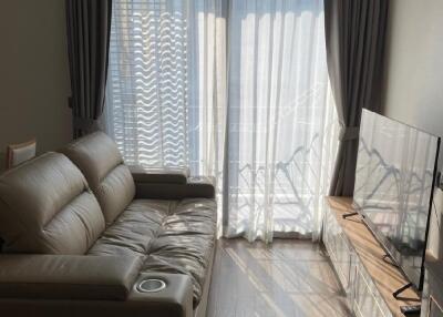 Living room with beige leather sofa, large window with sheer curtains, and wall-mounted TV