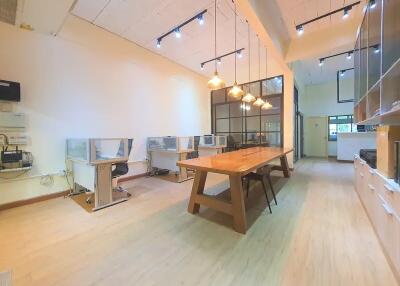 Spacious office room with long wooden table and chairs, workstations, and hanging lights