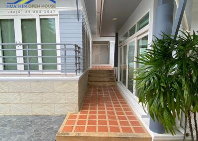 Exterior view of the building entrance showing a tiled walkway, railings, and a potted plant