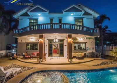Two-story house with balcony, patio, and lit-up pool area at night