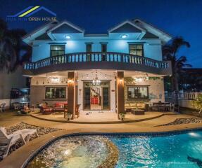 Two-story house with balcony, patio, and lit-up pool area at night