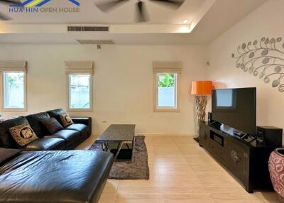 Modern living room with a black leather sofa, wall-mounted TV and ceiling fan