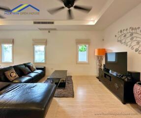 Modern living room with a black leather sofa, wall-mounted TV and ceiling fan