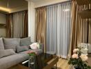 Living room with gray sofa, glass coffee table, and floor-to-ceiling curtains