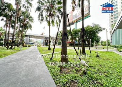 Exterior view of a landscaped garden with palm trees and modern infrastructure, including a billboard and skyscrapers in the background