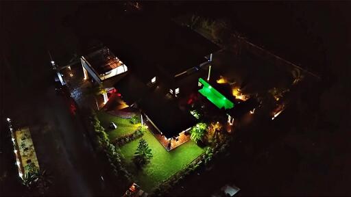 Night aerial view of a well-lit property with pool and garden