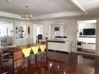 Dining area with wooden floors, modern dining table with green chairs, and adjacent living room with TV