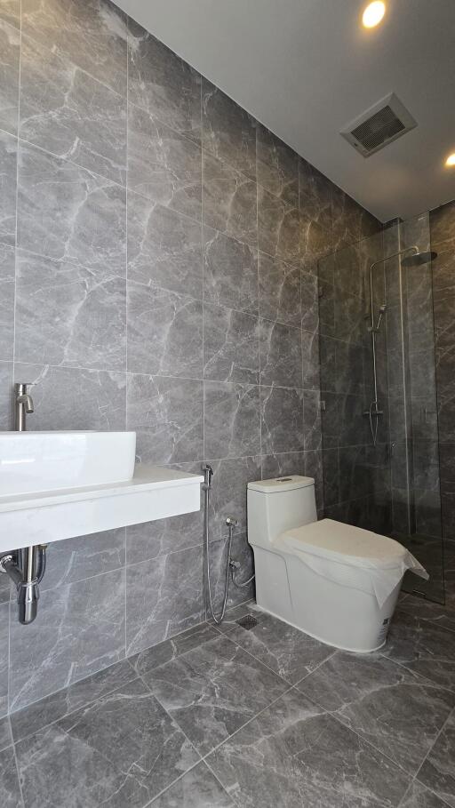 Modern bathroom with gray marble tiles, toilet, and walk-in shower