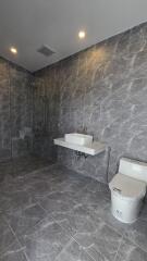 Spacious modern bathroom with tiled walls and floor, shower, sink, and toilet