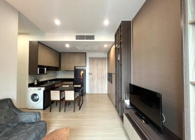 Modern living area with an open kitchen, dining table, washing machine, and television