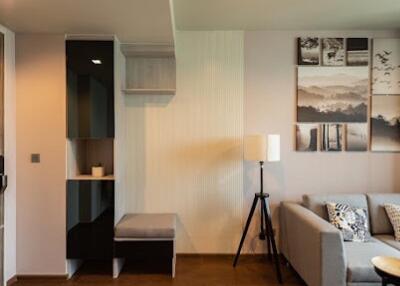 A modern living room with a gray sofa, shelving unit, floor lamp, and wall art.