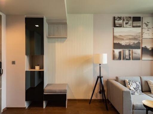 A modern living room with a gray sofa, shelving unit, floor lamp, and wall art.