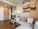 Modern living room with a light gray sectional sofa, decorative pillows, wall art, a floor lamp, and a small round table with a plant