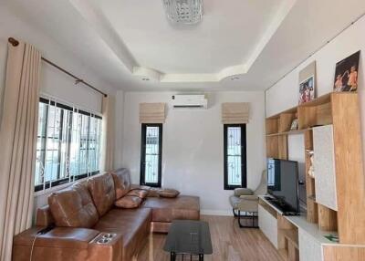 Cozy living room with brown leather sofa, modern lighting, wooden furniture, and large windows