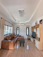 Cozy living room with brown leather sofa, modern lighting, wooden furniture, and large windows