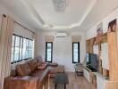 Cozy living room with brown leather sofa, modern lighting, wooden furniture, and large windows