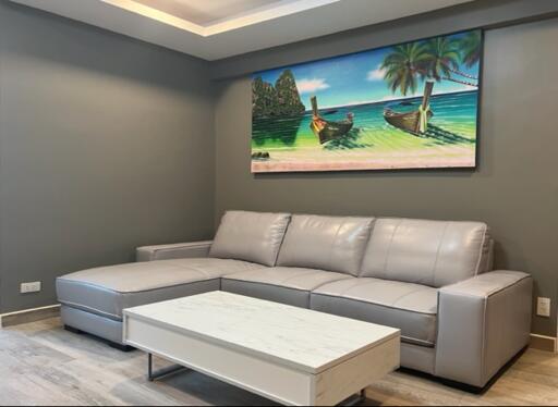 Modern living room with a gray sectional sofa and a tropical painting