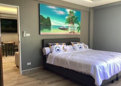 Bedroom with a large bed, tropical wall art, and adjacent living space