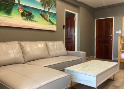 Comfortable living room with beige leather sofa and a tropical-themed painting above it, white coffee table