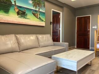 Comfortable living room with beige leather sofa and a tropical-themed painting above it, white coffee table