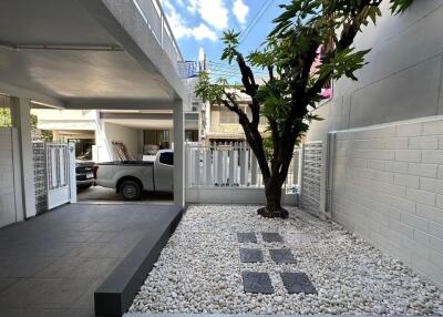 Outdoor area with driveway, partial view of the house, garden with tree and white stones