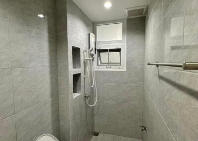 Modern bathroom with tiled walls and floors, featuring an open shower, toilet, and window.