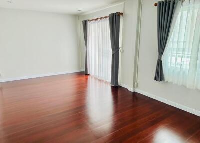 Spacious living room with hardwood floors and large windows with curtains