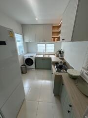 A modern kitchen with white cabinets, refrigerator, washing machine, sink, and gas stove