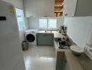 A modern kitchen with white cabinets, refrigerator, washing machine, sink, and gas stove