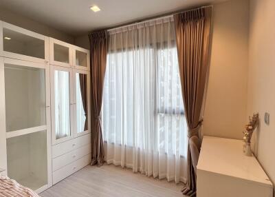 A well-furnished bedroom with a wardrobe, desk, and large window with curtains