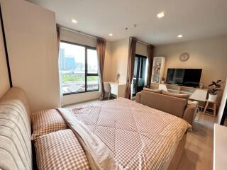 Modern bedroom with a view of the city, featuring a bed, sofa, TV, and large windows.